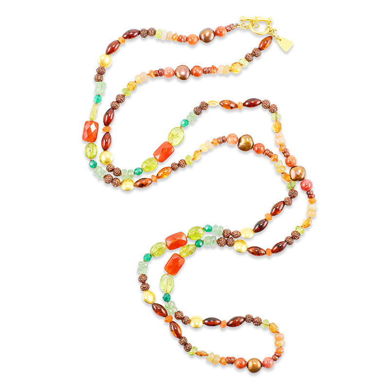 A long, multi-colored beaded necklace made with a variety of gemstones and seeds, including peridot, carnelian, and freshwater pearls, with an 18k gold clasp.