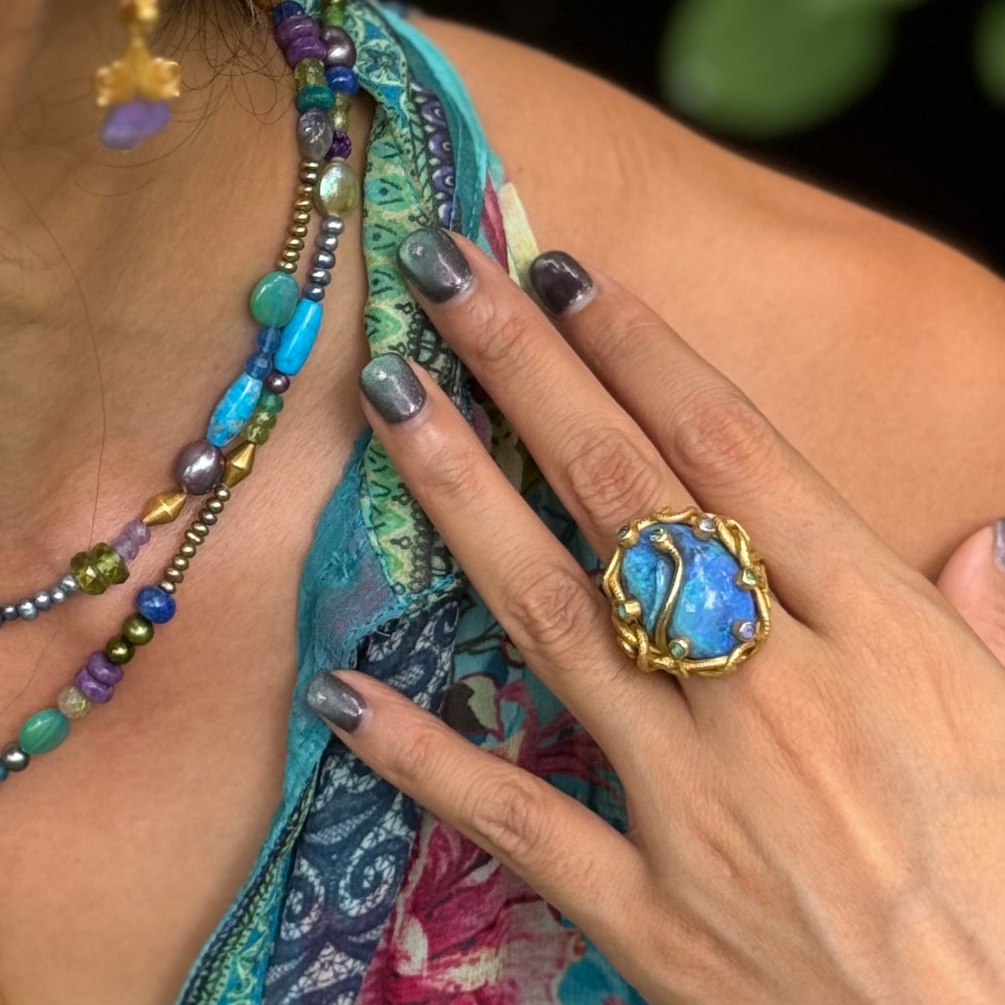 Close-up of a hand wearing a blue ring with gold accents, holding colorful beaded jewelry.