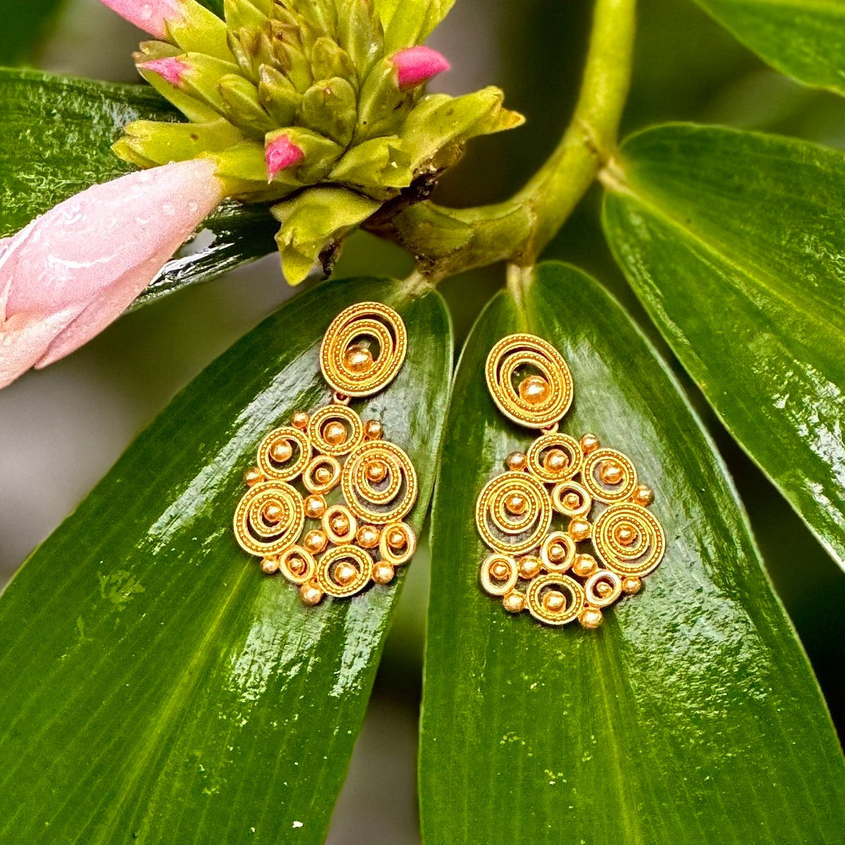Gold earrings on a green leaf with pink flowers