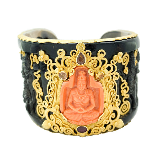 A black and orange coral cuff bracelet with gold details and a carved buddha motif in the center, accented with multicolored gemstones.