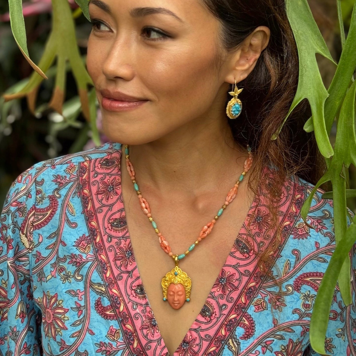 Woman wearing a colorful patterned top and necklace with a plant in the background