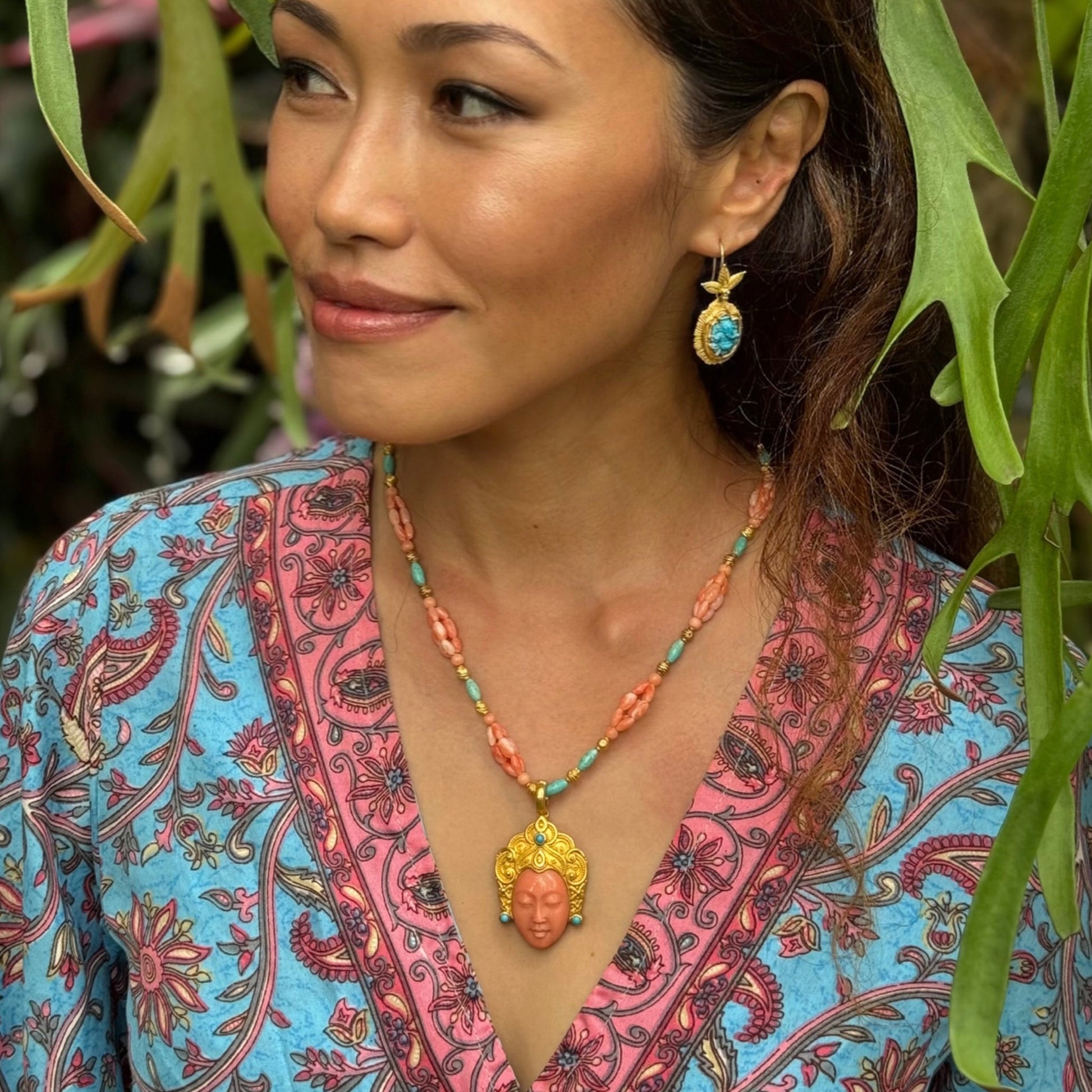 Woman wearing a colorful patterned top and necklace with a plant in the background