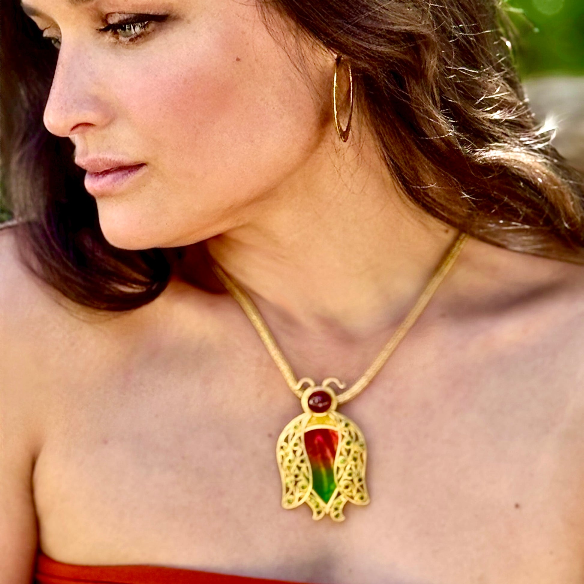 Woman wearing a gold necklace with a colorful pendant outdoors