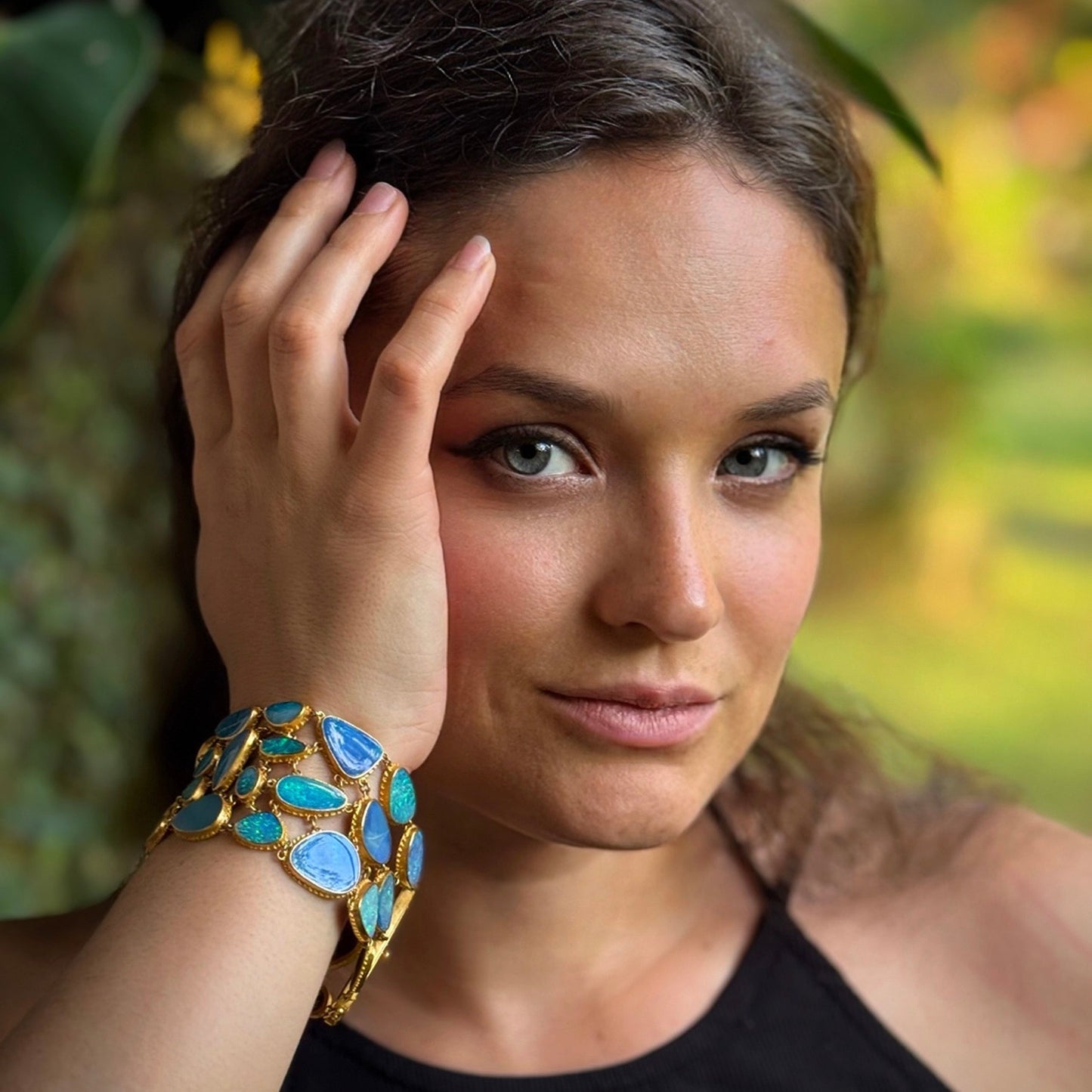Woman wearing a gold and blue bracelet with a blurred natural background