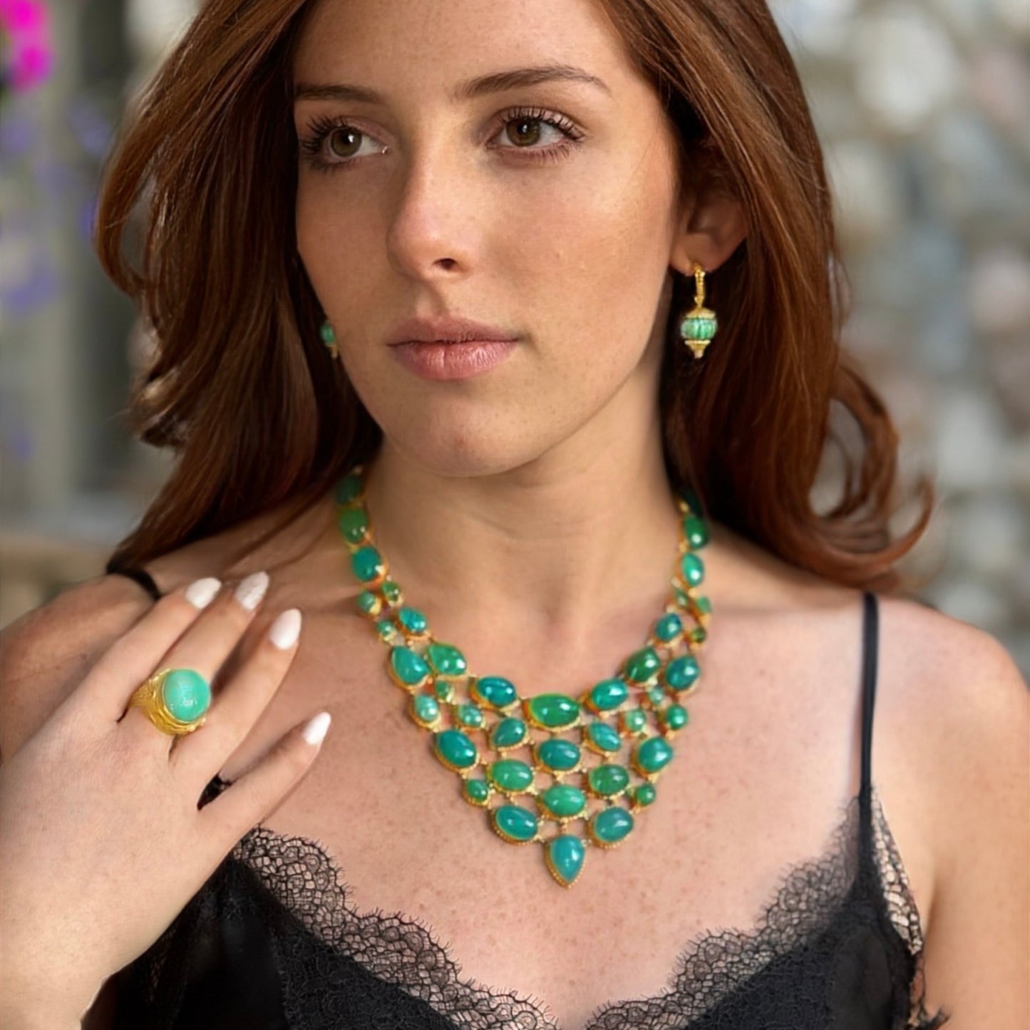Woman wearing a green and gold necklace and earrings with a blurred background