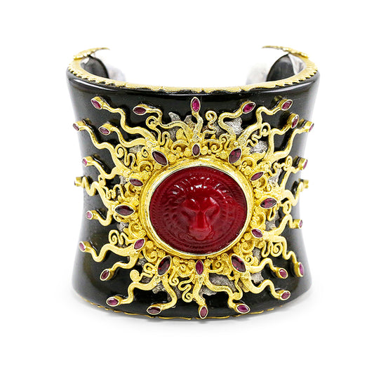 A luxurious hand-crafted cuff bracelet made from black Namibian buffalo horn, featuring a red Venetian glass centerpiece surrounded by gold and silver designs, with small rubies and a crimson Murano glass medallion.