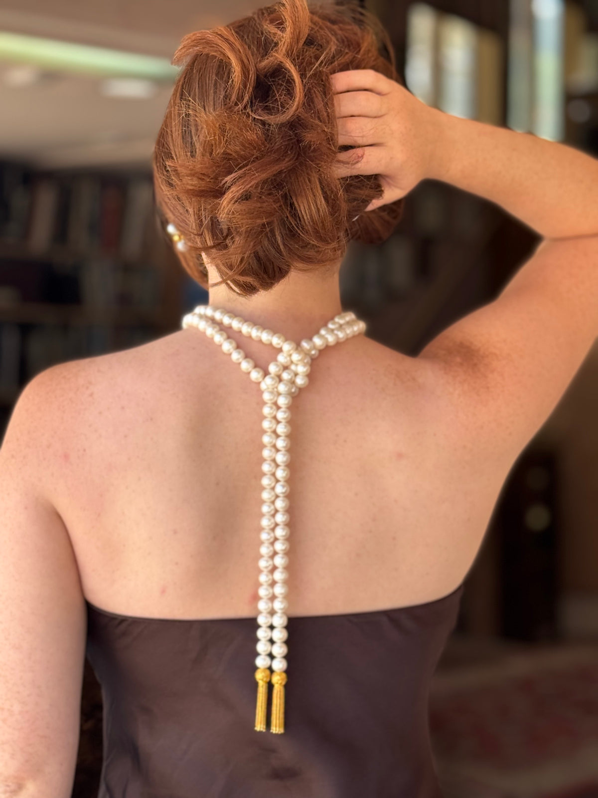 Woman with a pearl necklace draped over her shoulder against a blurred indoor background