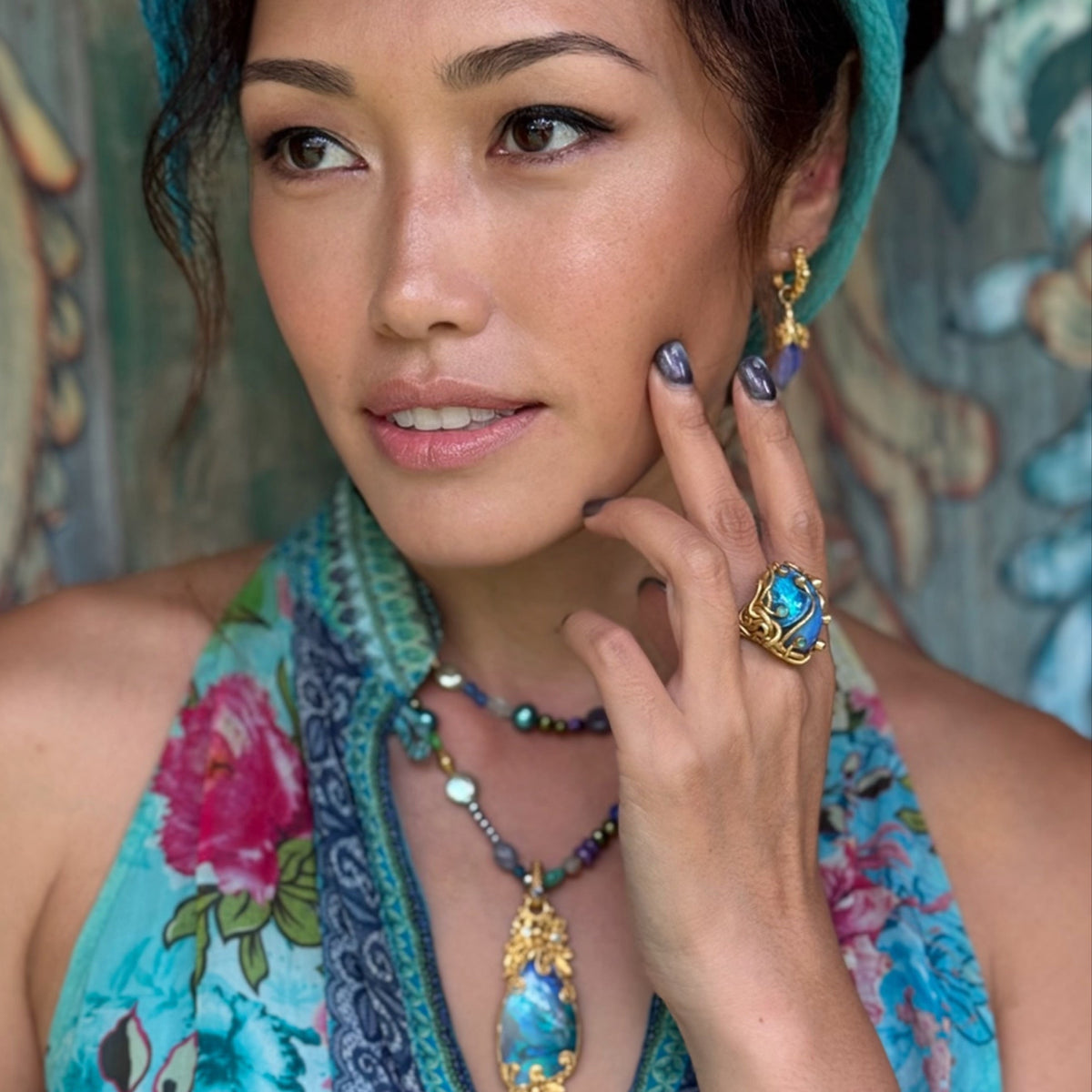 Woman wearing a colorful headscarf and floral dress with jewelry against a decorative background
