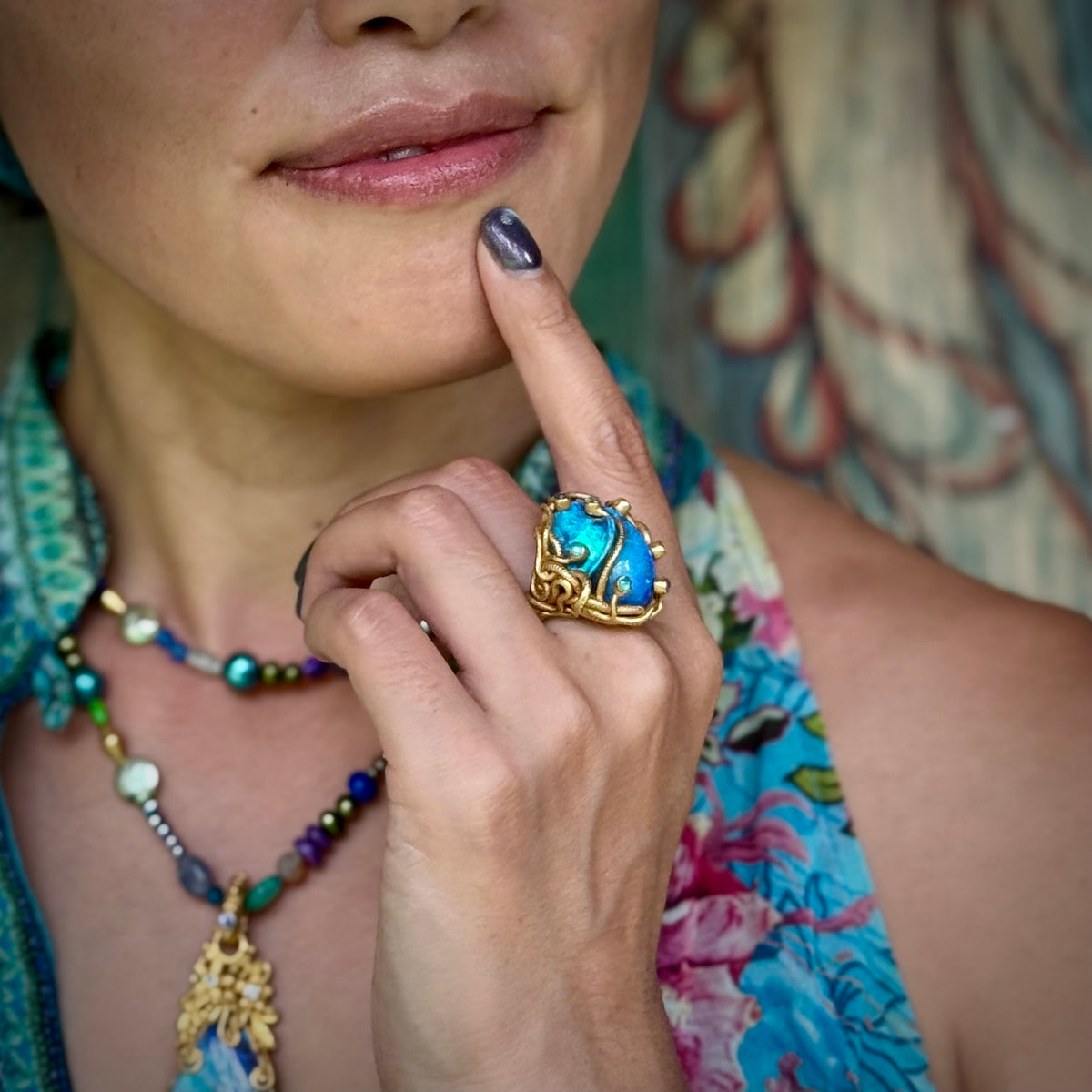 Close-up of a person wearing a colorful ring with a blue stone, surrounded by jewelry.