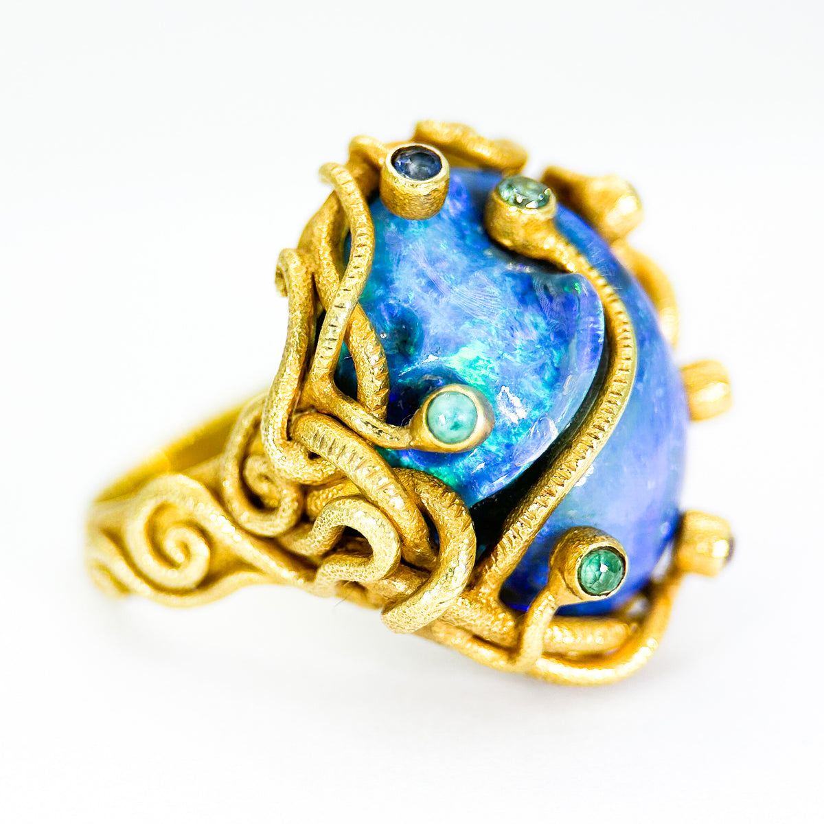 Gold ring with a blue gemstone and green accents on a white background