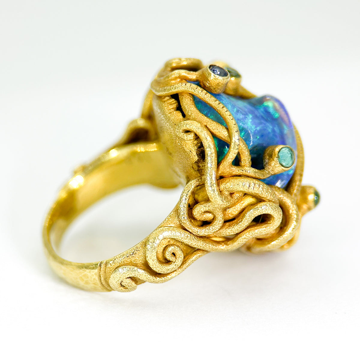 Gold ring with intricate design and blue gemstone on a white background