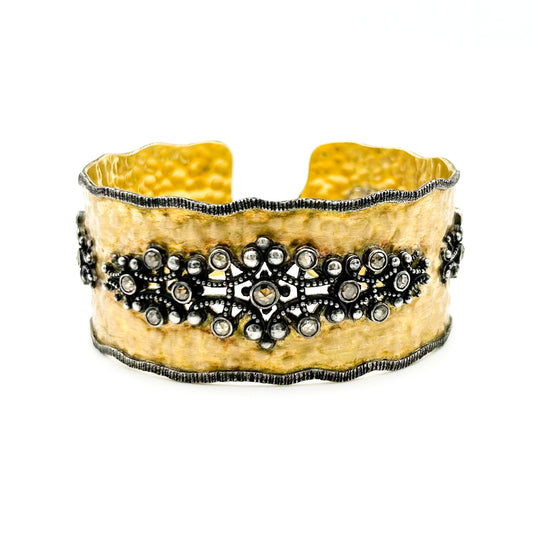 Wide gold bracelet with black decorative elements on a white background
