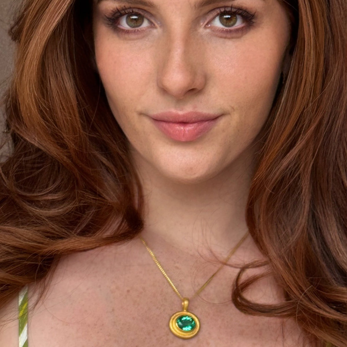 Woman wearing a gold necklace with a green gemstone pendant